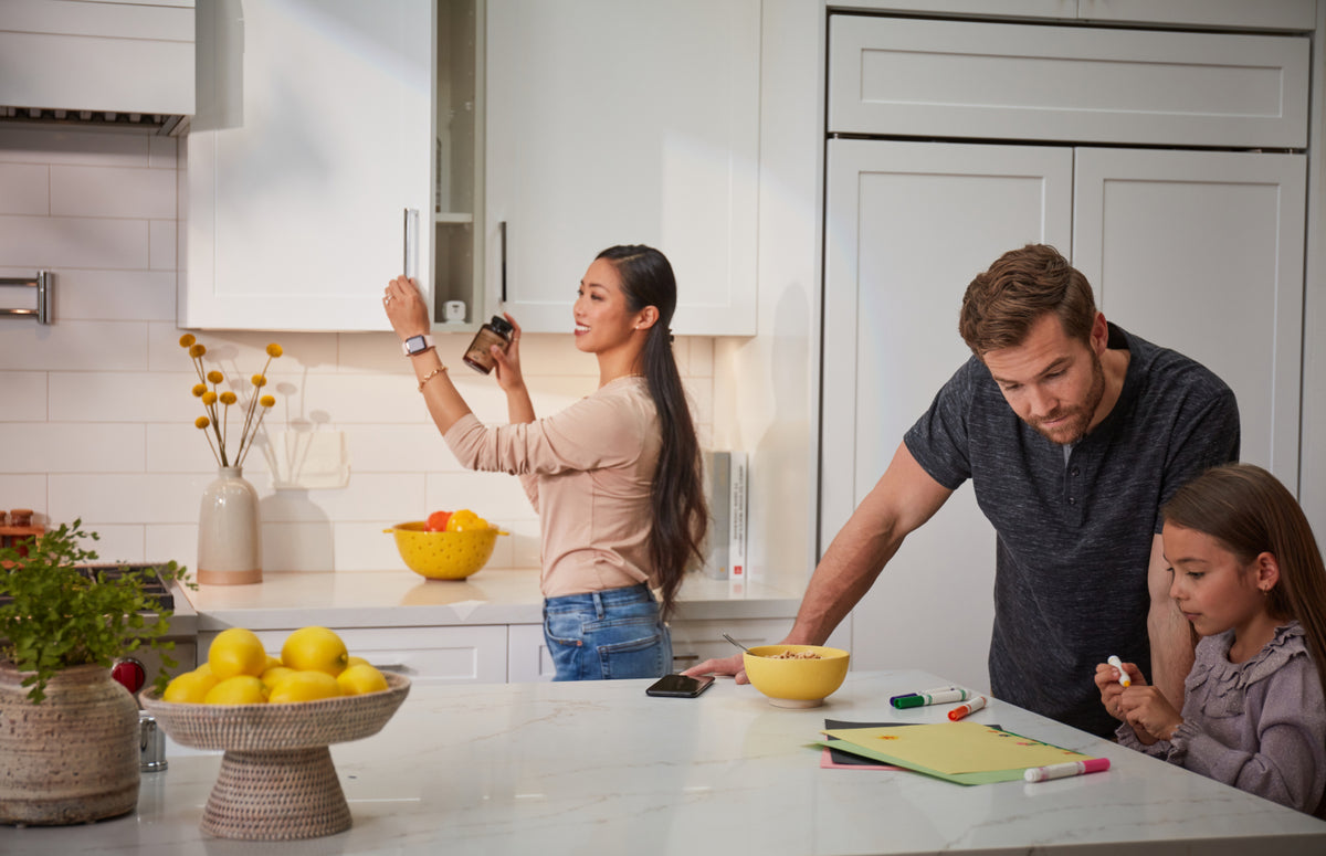 Woman retrieving medicine from cabinet while father and daughter do homework nearby